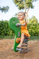 young girl plays on green spring rider in a playground