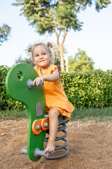 A young girl with blonde hair sits on a playground seesaw