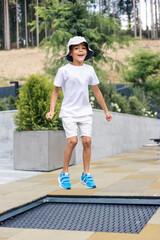 boy jumps on trampoline, wearing white t-shirt, shorts, bucket hat