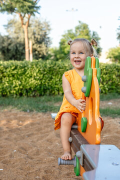 A young girl with blonde hair sits on a playground seesaw.