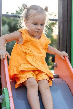 Young Caucasian girl with blonde hair sits on a playground slide