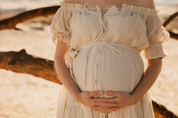 Pregnant woman in bohemian dress holding belly in dry grassy field