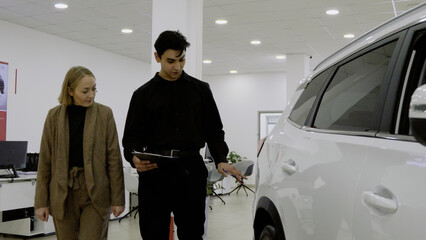 Happy couple and salesman next to a new white car, celebrating a deal