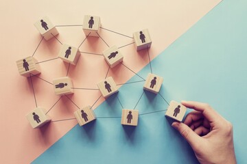 Connecting people in a network structure using wooden blocks with human icons on a split pink and blue background