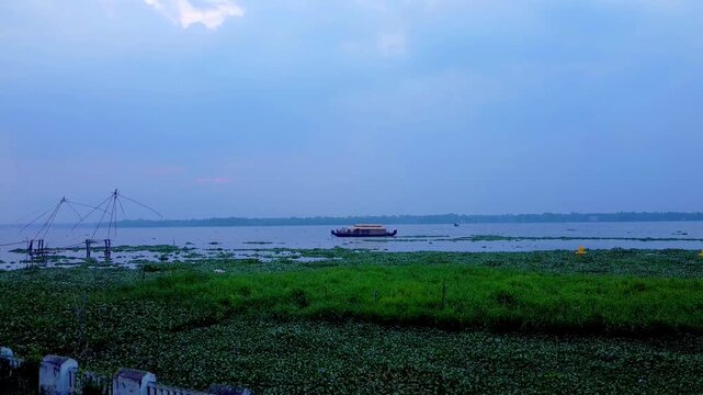 Houseboat and Chinese fishing net on Kerala backwaters at dusk with lush aquatic plants.