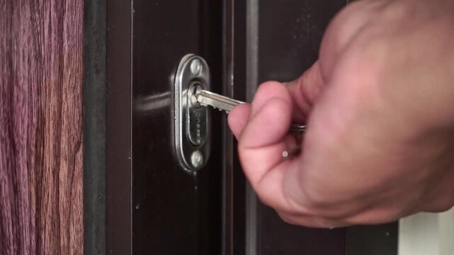 Hand reaching for a key inserted in a door lock and turning it to open a wooden door. Ideal for concepts of safety, access, and home living.