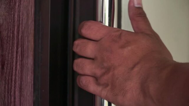 Close-up shot of a hand gripping a metal door handle and opening a wooden door. The scene captures everyday home activity with natural lighting.