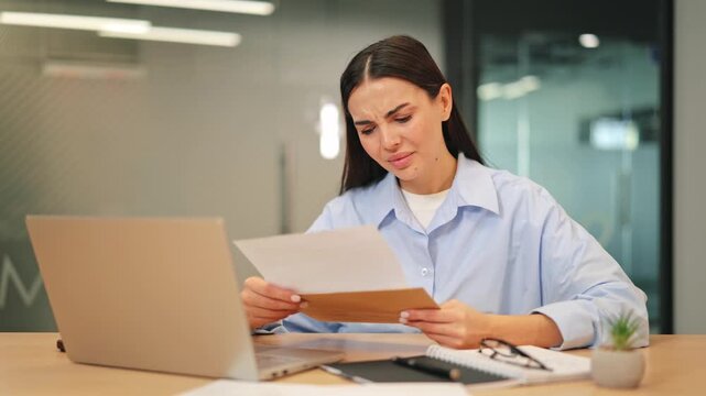 Young professional reads important document, initially calm. Expression shifts to worried, sad, shocked. Displays disappointment and emotional distress receiving bad news in modern office environment.