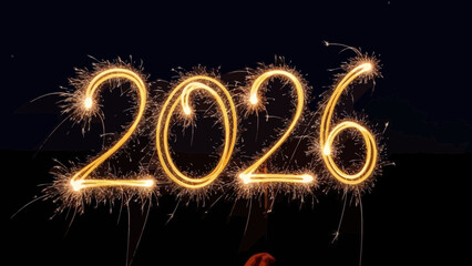 Glowing yellow fireworks spelling out twenty twenty six in night sky with sparks