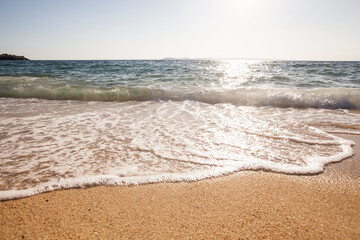 Gentle waves crash onto a wet sandy beach, sparkling under the sunlight