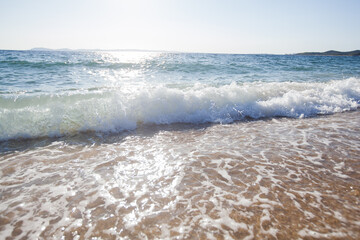 Gentle waves crash onto a wet sandy beach, sparkling under the sunlight