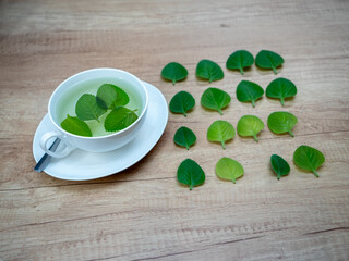 A cup of herbal tea with Indian borage leaves on a wooden surface, with fresh leaves beside the cup prepared for use.