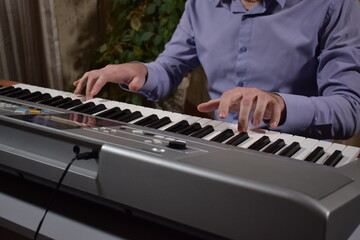 A young white man plays an electronic synthesizer indoors, immersed in his creative hobby. Focused on shaping tones and melodies, he explores musical expression and artistry in a calm home setting.

