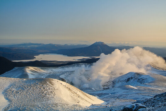 A stunning winter view from Mount Meakan captures rising volcanic steam, snow covered ridges, Lake Akan below, and the iconic silhouette of Mount Oakan under the calm morning sky
