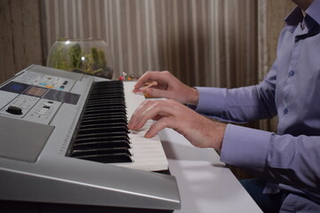 A young white man plays an electronic synthesizer indoors, immersed in his creative hobby. Focused on shaping tones and melodies, he explores musical expression and artistry in a calm home setting.
