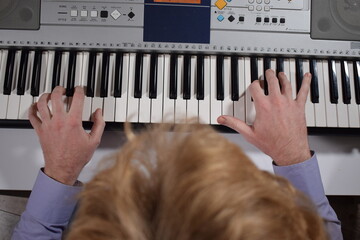 A young white man plays an electronic synthesizer indoors, immersed in his creative hobby. Focused on shaping tones and melodies, he explores musical expression and artistry in a calm home setting.
