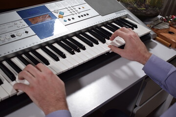 A young white man plays an electronic synthesizer indoors, immersed in his creative hobby. Focused...