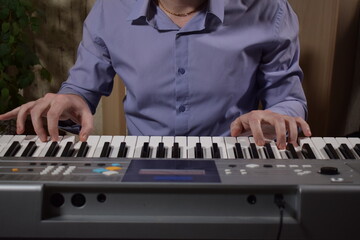 A young white man plays an electronic synthesizer indoors, immersed in his creative hobby. Focused on shaping tones and melodies, he explores musical expression and artistry in a calm home setting.
