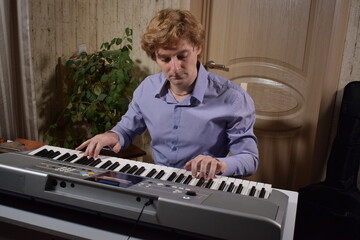 A young white man plays an electronic synthesizer indoors, immersed in his creative hobby. Focused on shaping tones and melodies, he explores musical expression and artistry in a calm home setting.
