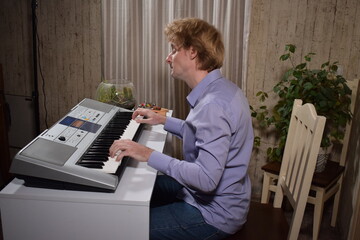 A young white man plays an electronic synthesizer indoors, immersed in his creative hobby. Focused on shaping tones and melodies, he explores musical expression and artistry in a calm home setting.
