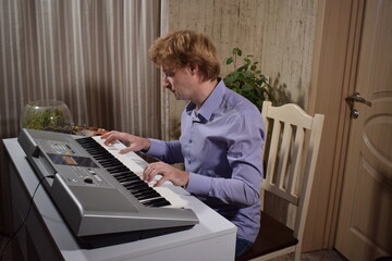 A young white man plays an electronic synthesizer indoors, immersed in his creative hobby. Focused on shaping tones and melodies, he explores musical expression and artistry in a calm home setting.
