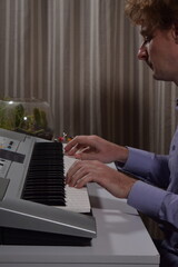 A young white man plays an electronic synthesizer indoors, immersed in his creative hobby. Focused on shaping tones and melodies, he explores musical expression and artistry in a calm home setting.

