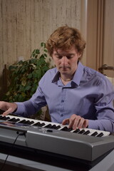 A young white man plays an electronic synthesizer indoors, immersed in his creative hobby. Focused on shaping tones and melodies, he explores musical expression and artistry in a calm home setting.
