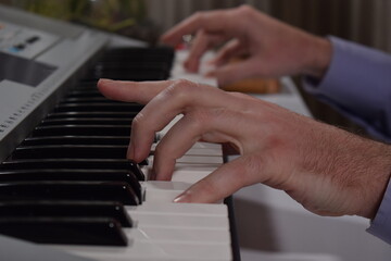A young white man plays an electronic synthesizer indoors, immersed in his creative hobby. Focused on shaping tones and melodies, he explores musical expression and artistry in a calm home setting.
