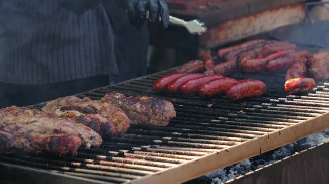 Close-up of grilling sausages and beef on an outdoor barbecue grill in summer, preparing over smoky charcoal. Picnic time with an outdoor grill party.