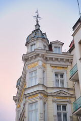 Obraz premium Ornate art nouveau building facade showcasing architectural details, a corner tower with a decorative metal finial, and gilded stucco ornaments against a soft gradient sky