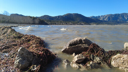 On a windy day, stormy lake water and muddy algae on the shore in a mountainous area. The power of nature and pollution.
