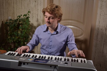A young white man plays an electronic synthesizer indoors, immersed in his creative hobby. Focused on shaping tones and melodies, he explores musical expression and artistry in a calm home setting.
