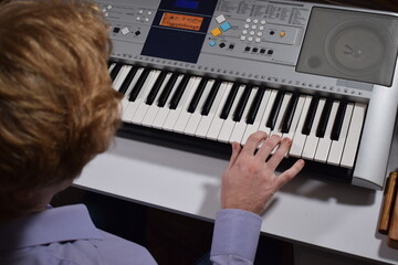 A young white man plays an electronic synthesizer indoors, immersed in his creative hobby. Focused on shaping tones and melodies, he explores musical expression and artistry in a calm home setting.

