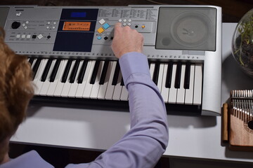 A young white man plays an electronic synthesizer indoors, immersed in his creative hobby. Focused on shaping tones and melodies, he explores musical expression and artistry in a calm home setting.
