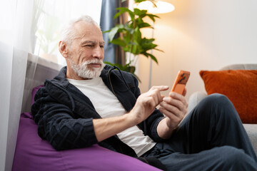 Senior man relaxing at home, enjoying modern technology with smartphone