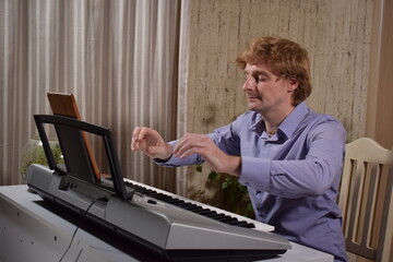 A young white man plays an electronic synthesizer indoors, immersed in his creative hobby. Focused on shaping tones and melodies, he explores musical expression and artistry in a calm home setting.
