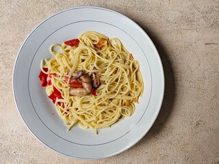 Spaghetti with Indonesian-style seasoning, squid chili sauce, served on a white plate, isolated on a beige background.