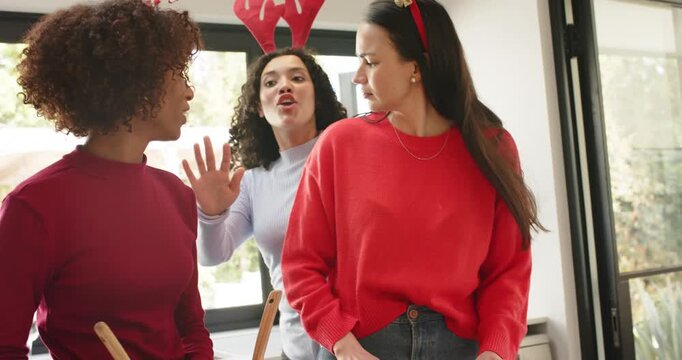 Diverse female friends mixing salad on kitchen island, friend tapping shoulder sparking caroling