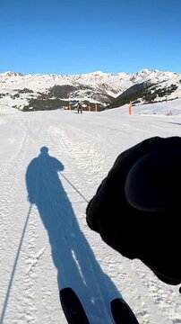 Thrilling first person view of a skier going down a perfectly groomed slope at a mountain resort, with a long shadow projected on the fresh snow under a clear blue sky on a sunny day