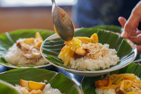 Close-up of traditional Indonesian chicken rice being served with vegetables and eggs on a banana leaf plate. Authentic Asian cuisine, warm natural lighting, and vibrant colors