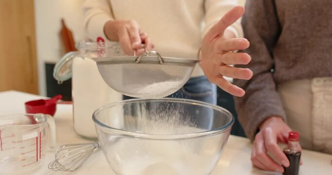 With sugar in sieve, person is shaking, tapping it to sift sugar into bowl on counter