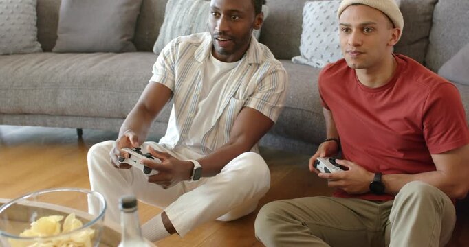 Diverse male friends picking up wireless controllers, pressing buttons to compete in living room