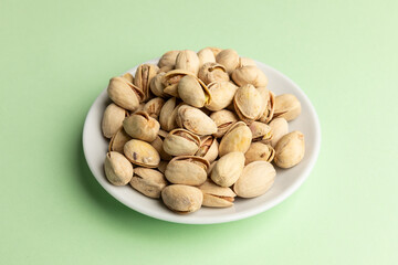 Small plate of pistachios isolated on light green background