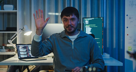 Adult male freelance programmer work late speak in online meeting video conference and looking at camera in tech office night. Artificial intelligence, robotics, user interface, machine learning.