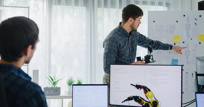 Team adult male engineer develop present AI robotics hand project at tech workspace. Artificial intelligence, collaboration support prototype development, robotic, debugging, machine learn, training.