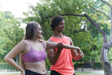 Personal trainer helping woman stretching arm in park