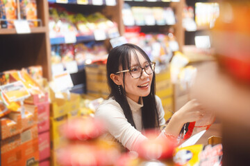 Young adult asian woman customer choosing snack food from shelf shopping at asia supermarket