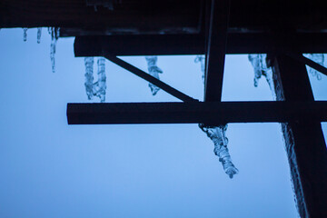 Icicles hanging from the eaves of the house. Frozen rain on the house. Dangerous icicles. Winter.