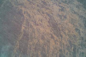 Top-down aerial view of abstract streaked ground texture with tan and orange colors. Fragmented geological surface pattern.