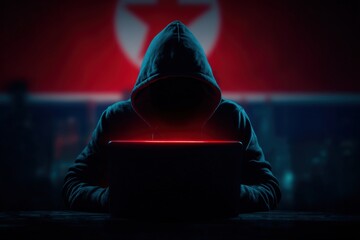 Hooded figure working on laptop with glowing screen in dark environment, symbolizing cybersecurity threats and digital espionage in a modern technological landscape